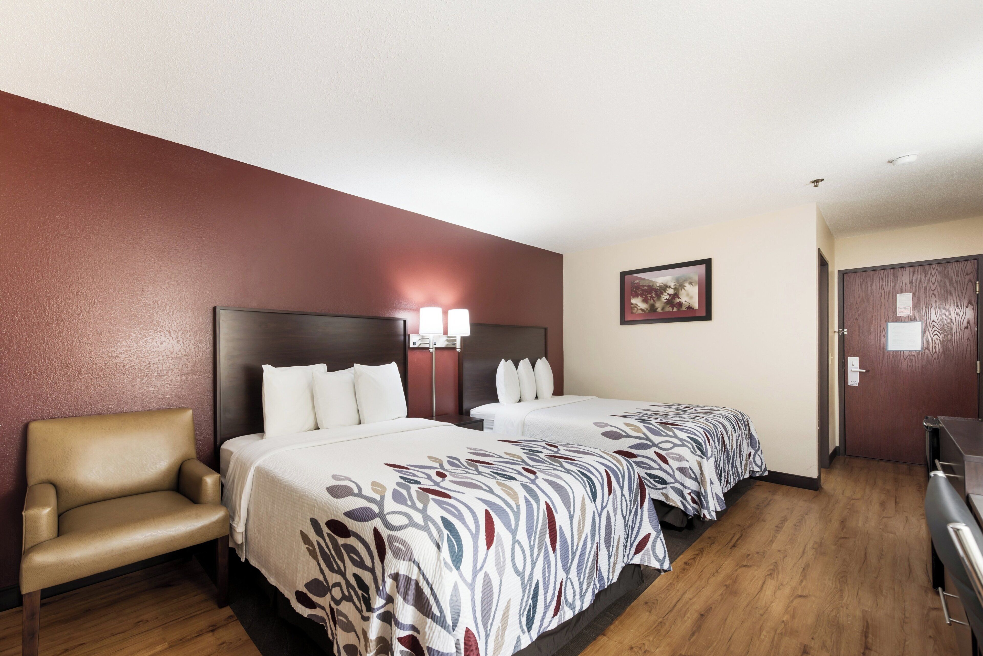 A hotel room with two beds, a chair, a desk, and a painting on the wall.