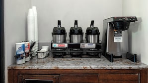 Un coin café équipé de trois machines à café, d’un distributeur d’eau chaude et d’une pile de tasses blanches.