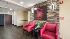 A Red Roof Inn lobby with two red leather chairs, a small table with a phone and a plant, and a stone wall with an exit sign. - Red Roof Inn Auburn (Auburn)