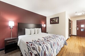 A hotel room with a large bed, two bedside tables, a nightstand, a wall-mounted lamp, and a framed picture. - Red Roof Inn Auburn (Auburn)