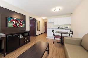 A compact living space with a flat-screen TV, a kitchenette, a dining area, and a sofa. - Red Roof Inn Auburn (Auburn)