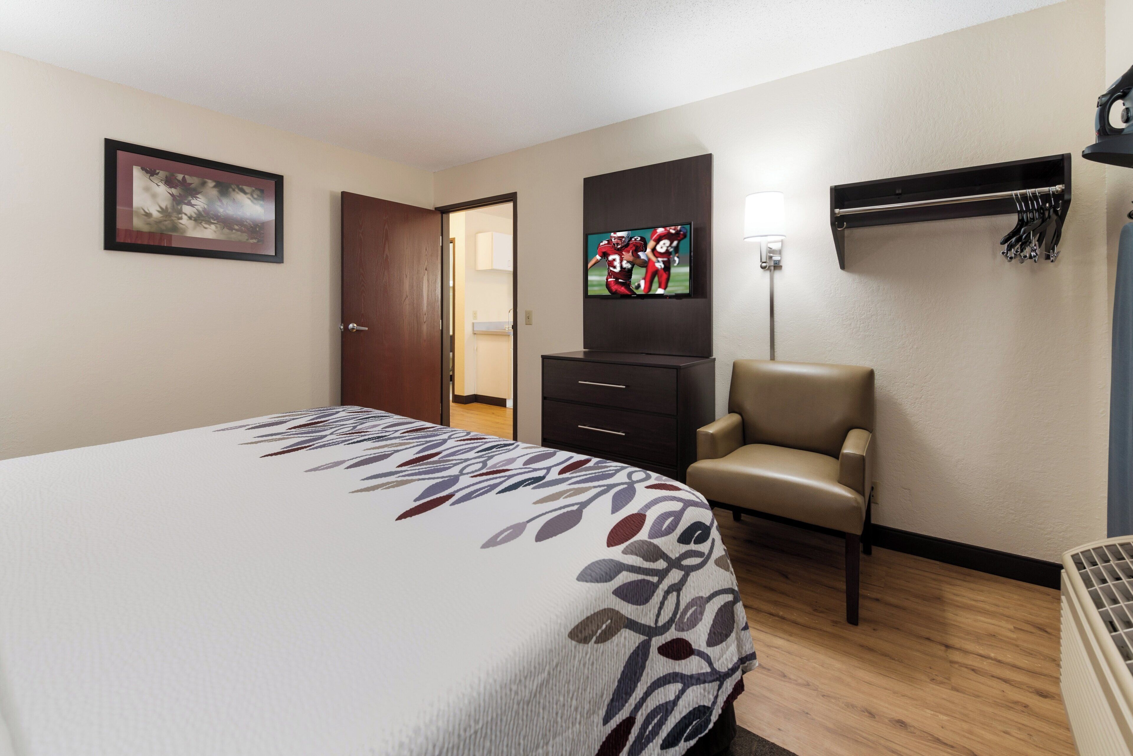 Habitación de hotel con una cama, televisión, una silla y una puerta que da a un baño.