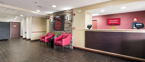 Zona de recepción de un hotel con un letrero de Red Roof Inn, un detector de incendios y un cartel de Wi-Fi gratuito.