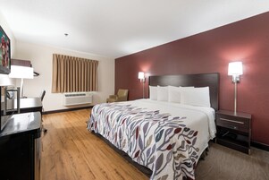 Habitación de hotel con cama, escritorio, silla, lámpara y calentador de pared.