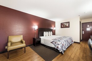 A hotel room with a bed, a chair, a nightstand, a desk, and a door. - Red Roof Inn Auburn (Auburn)