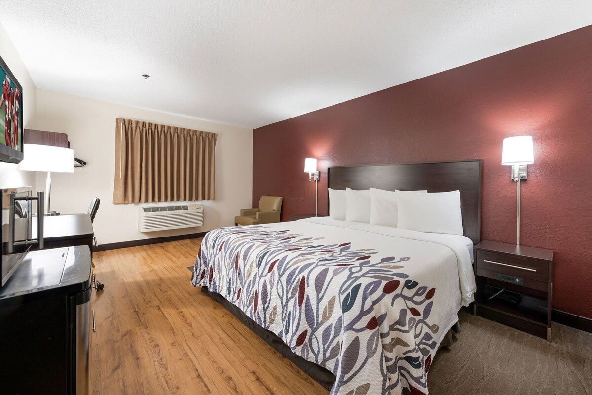 A hotel room with a bed, bedside tables, a desk, a chair, a lamp, and a window with curtains.