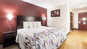 A hotel room with a large bed, two bedside tables, a nightstand, a wall-mounted lamp, a framed picture, and a door.