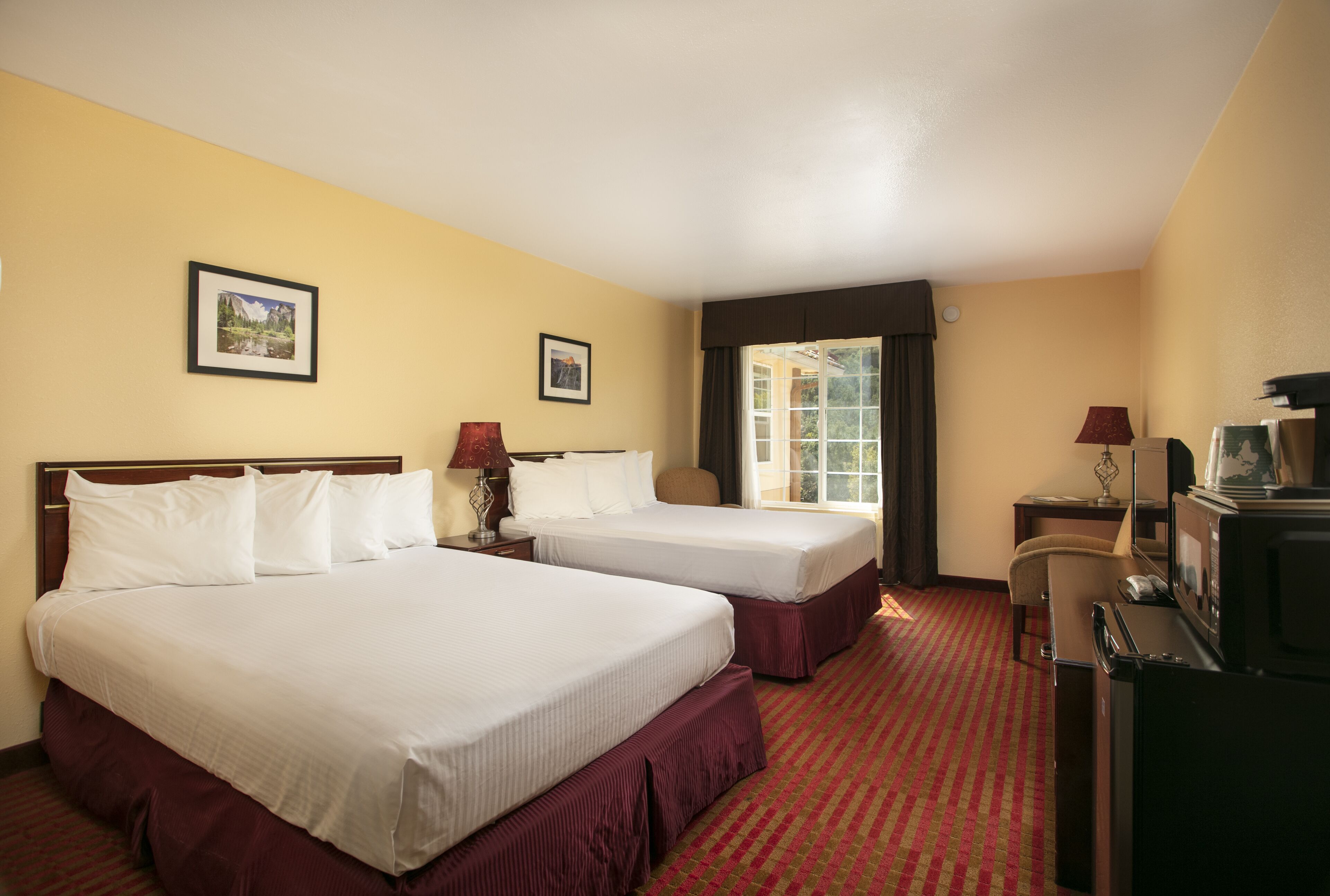 A hotel room with two beds, a TV, a desk, and a window with curtains.