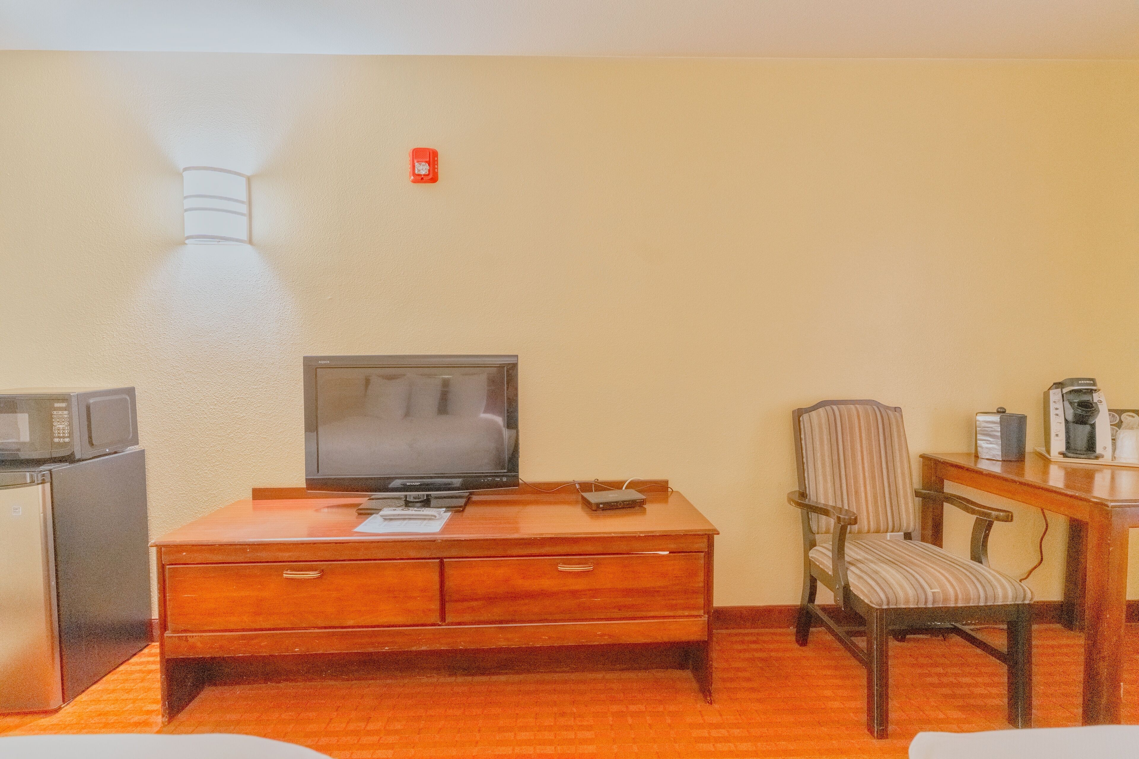 A hotel room with a wooden dresser, a television, a microwave, a coffee maker, and a striped chair.
