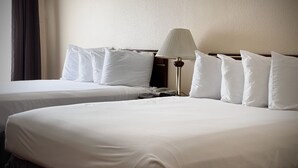 Two single beds with white linens, a bedside lamp, and a telephone on the left bed.