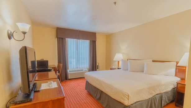 A hotel room with a large bed, a desk with a television, a lamp, and a window with curtains.