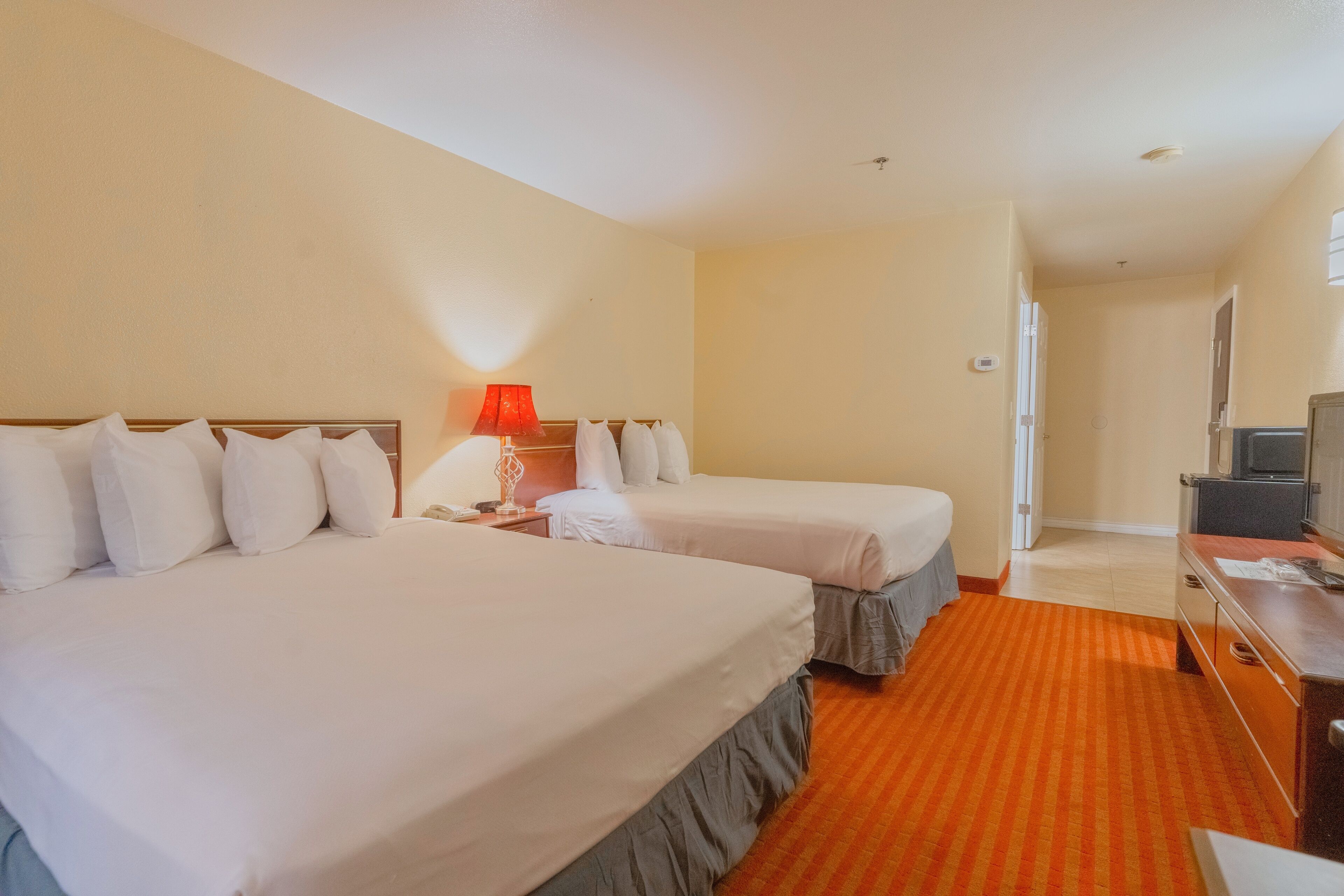 A hotel room with two beds, a TV, a desk, and a red carpet.