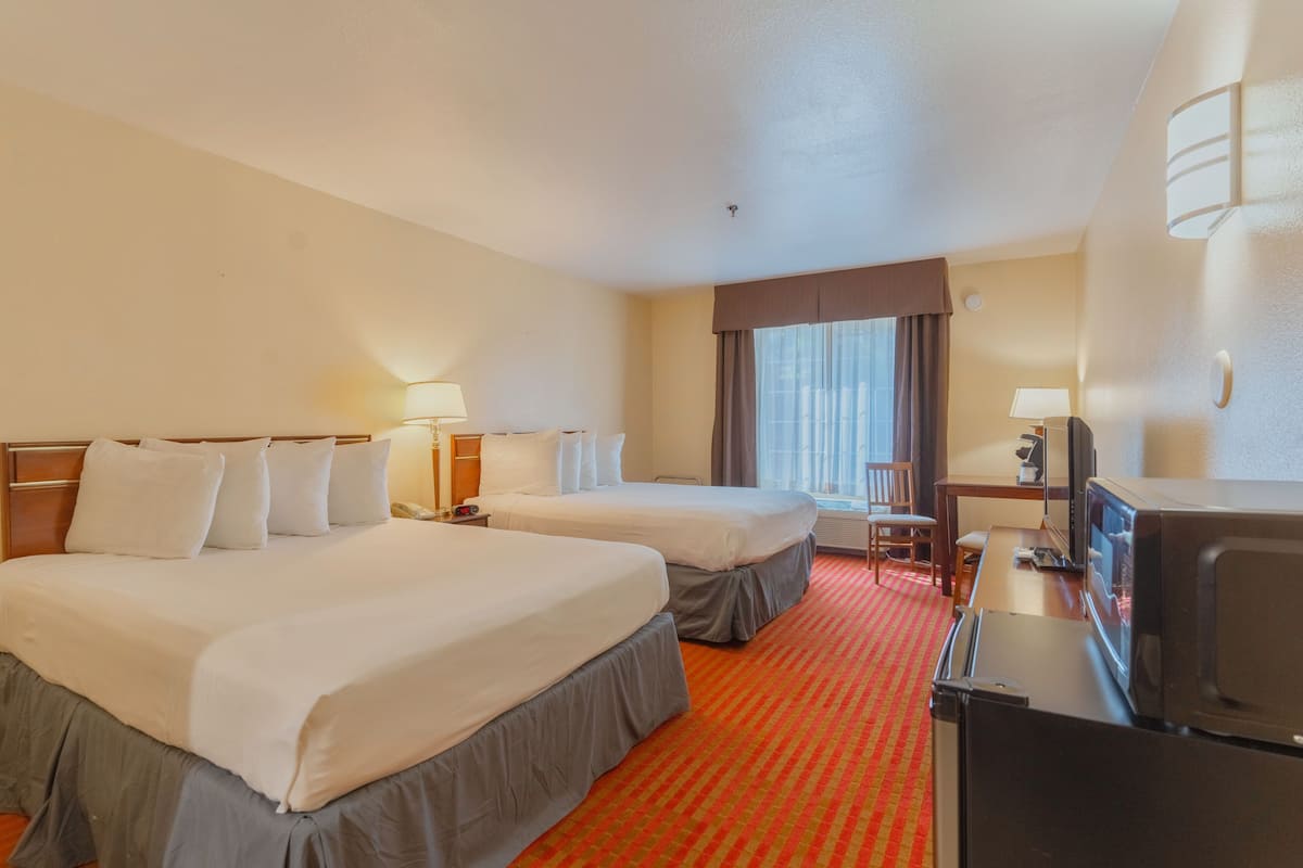 Habitación de hotel con dos camas, un escritorio, un televisor y una ventana con cortinas.
