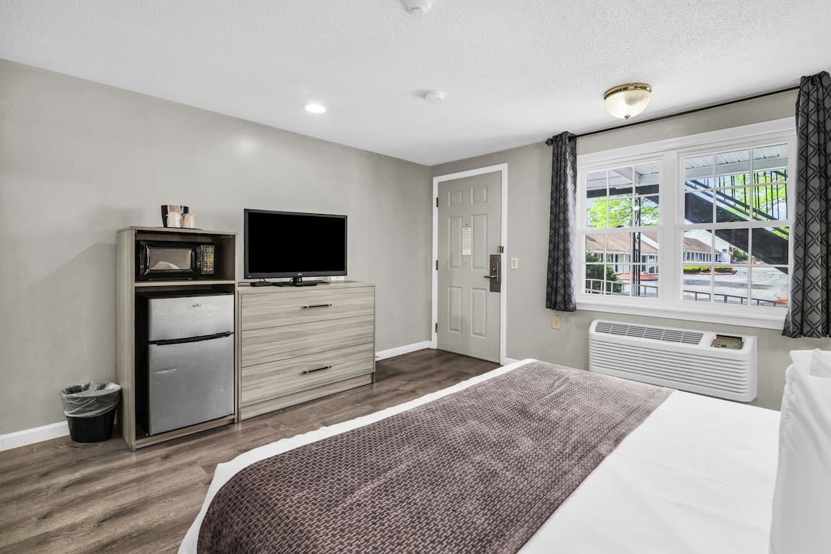 Habitación de hotel con cama, televisión, minibar, puerta y ventana con vista a un edificio.