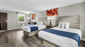 A hotel room with two beds, a desk, a chair, a window, and artwork on the walls.