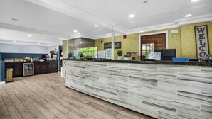 A reception area with a marble counter, a 'Welcome' sign, a 'Be Our Guest' sign, a Wi-Fi sign, and a view of the outdoors.
