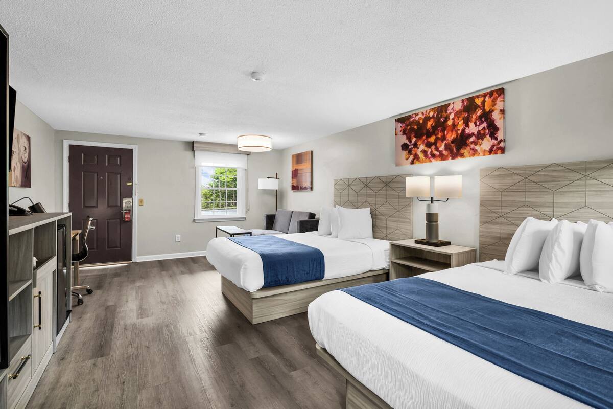 Habitación de hotel con dos camas, un escritorio, una silla, un armario y una ventana.