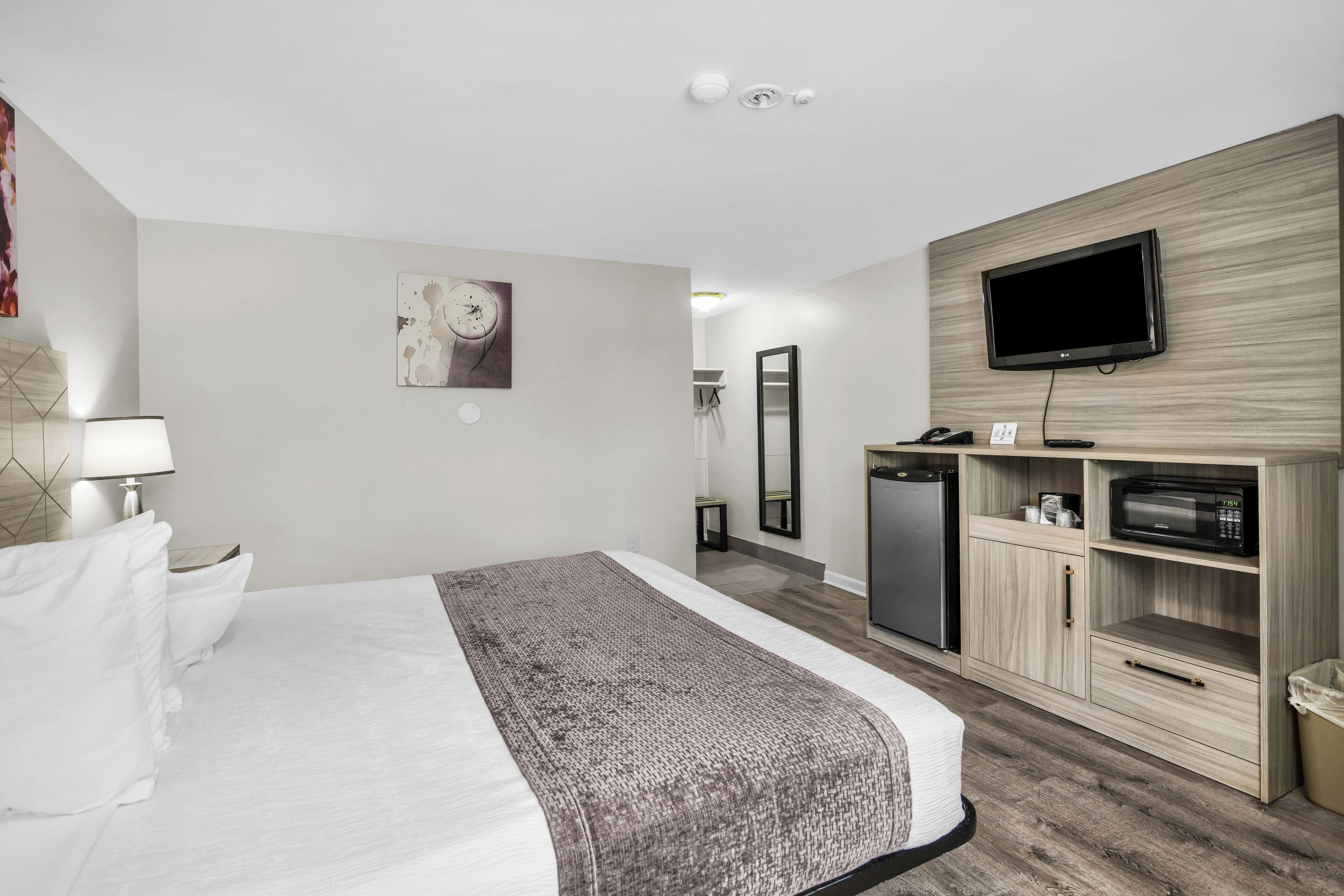 A hotel room with a bed, a television, a microwave, a refrigerator, and a mirror.