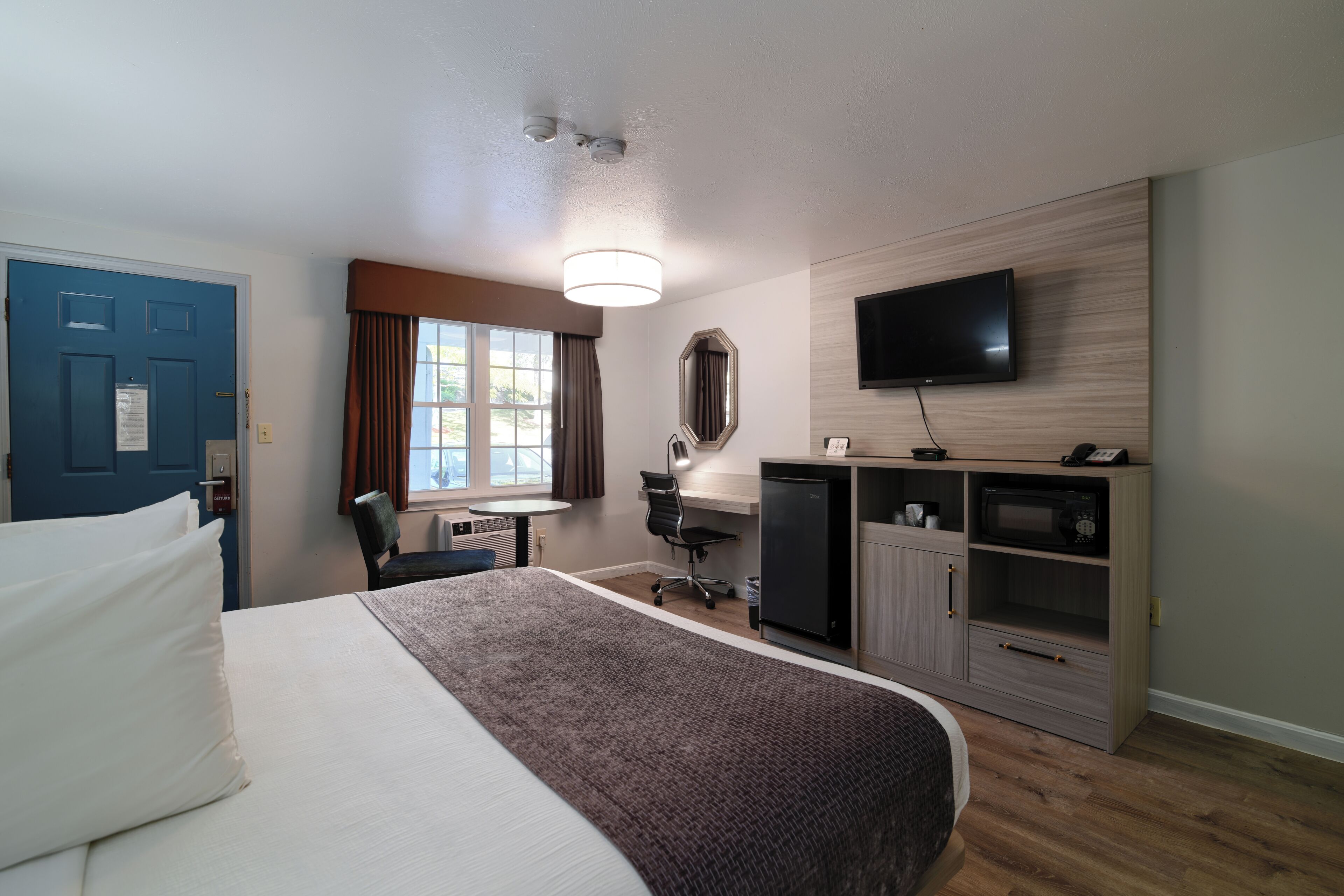 A hotel room with a bed, desk, chair, television, and a minibar.