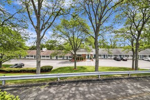 A motel with a parking lot, several trees, and a building with a sloped roof. - The Northshore Hotel - Boston/Danvers (Danvers)