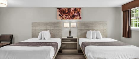 Habitación de hotel con dos camas, una mesita de noche con lámpara, una obra de arte geométrica en la pared y una ventana con cortinas.