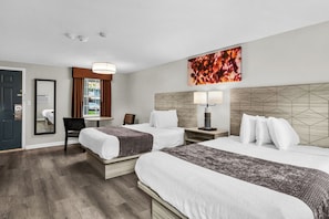 Habitación de hotel con dos camas, un escritorio, una silla, un ventanal grande y un cuadro en la pared.