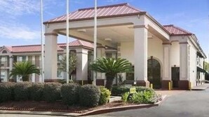 A hotel with a covered outdoor area, palm trees, and a well-maintained garden.