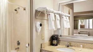 A bathroom with a shower, a sink, a coffee maker, and a towel rack with towels.