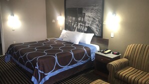A hotel room with a large bed, two bedside lamps, a striped armchair, and a painting on the wall.