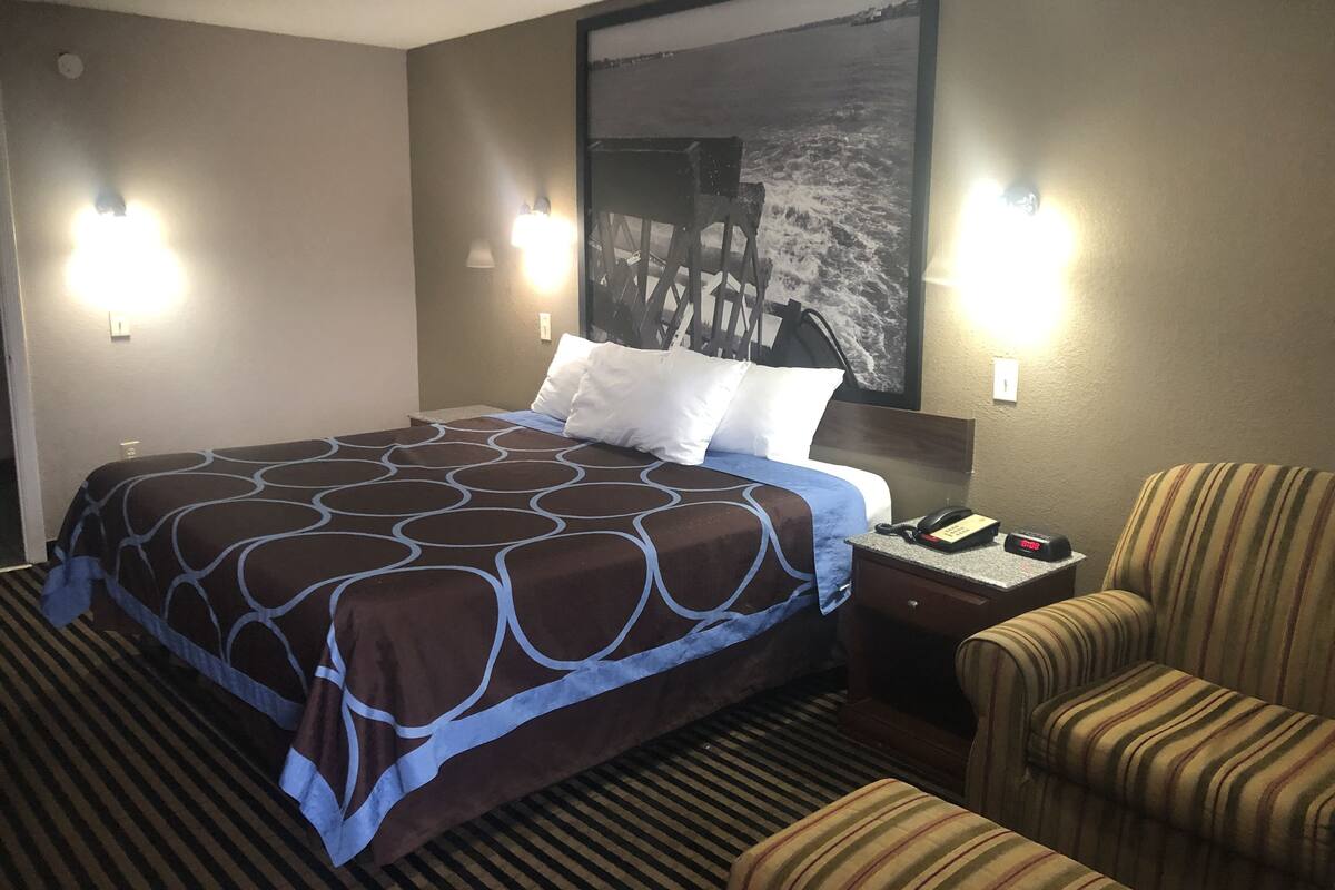Habitación de hotel con una cama grande, dos lámparas de noche, un sillón a rayas y un cuadro en la pared.