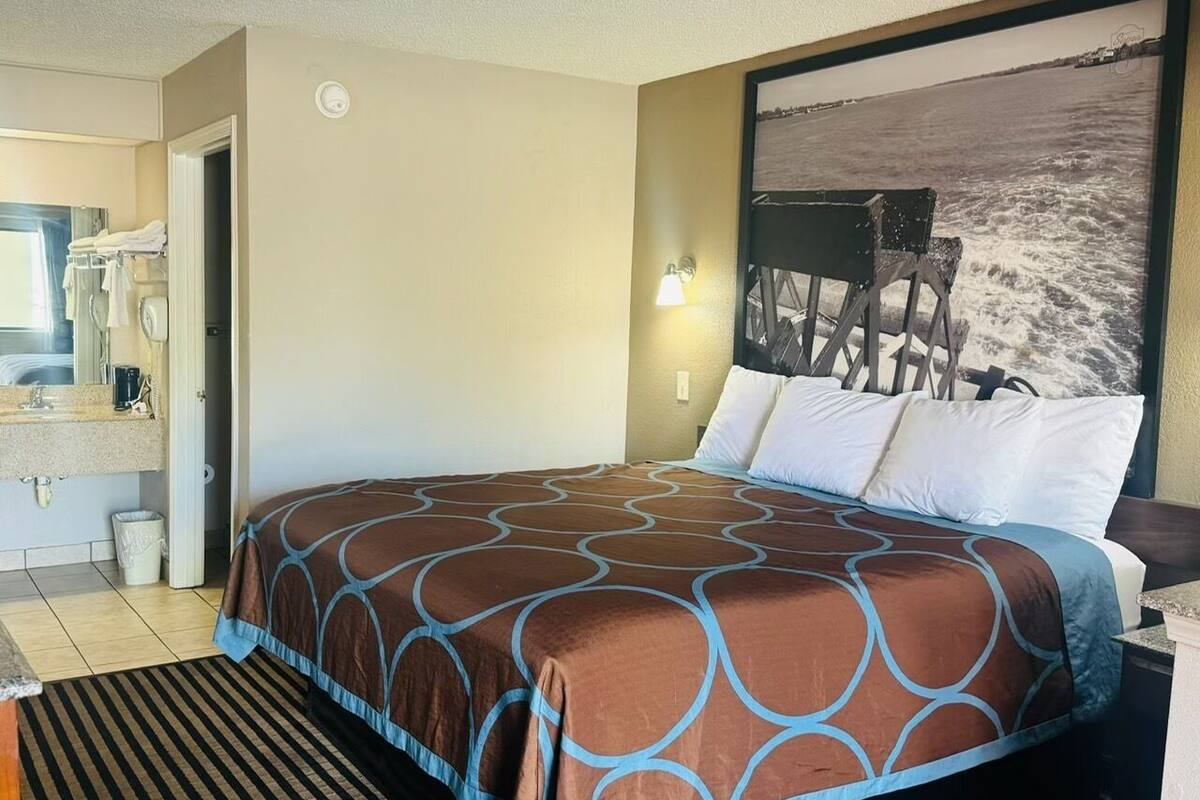 Habitación de hotel con una cama grande, un baño con lavamanos y espejo, y una lámpara fijada a la pared.