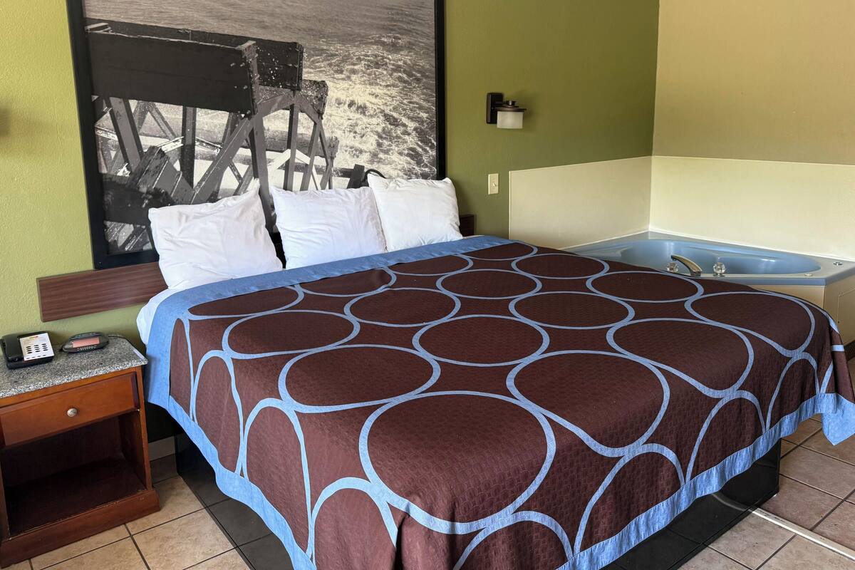 Habitación de hotel con una cama grande, una mesita de noche, una lámpara de pared y una bañera.
