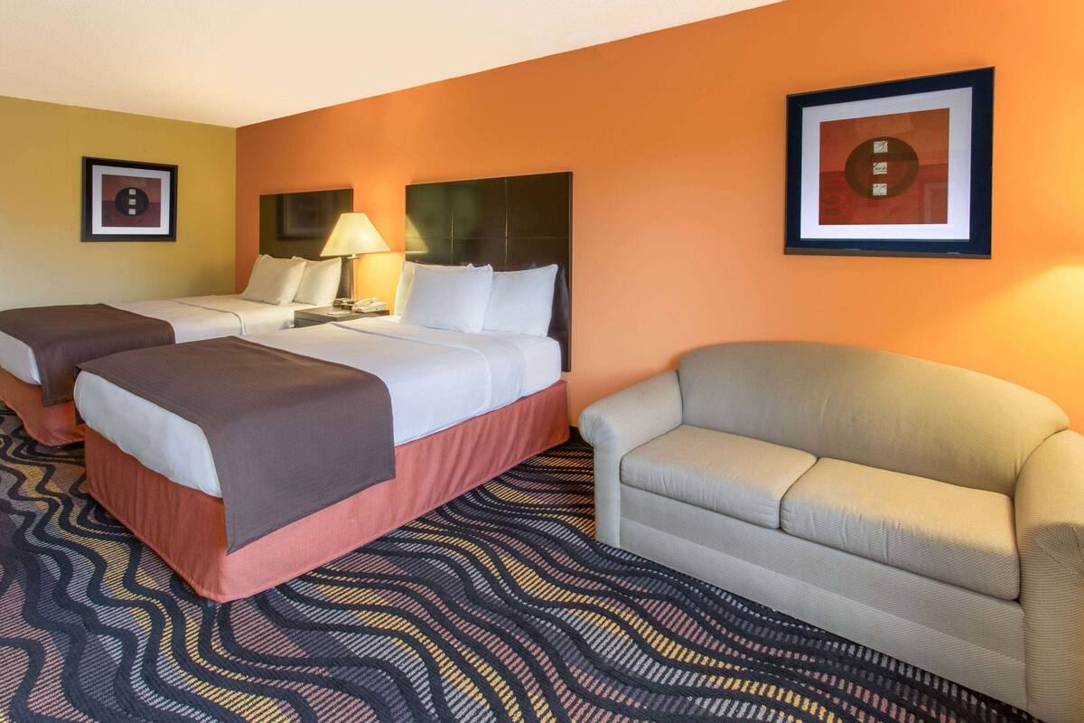 Une chambre d’hôtel avec deux lits, un canapé, une moquette à motifs et des tableaux encadrés aux murs.
