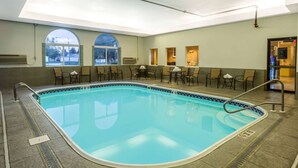 A swimming pool with a tiled deck, sunroof windows, and seating areas with tables and chairs. - AmericInn by Wyndham Streator (Streator)