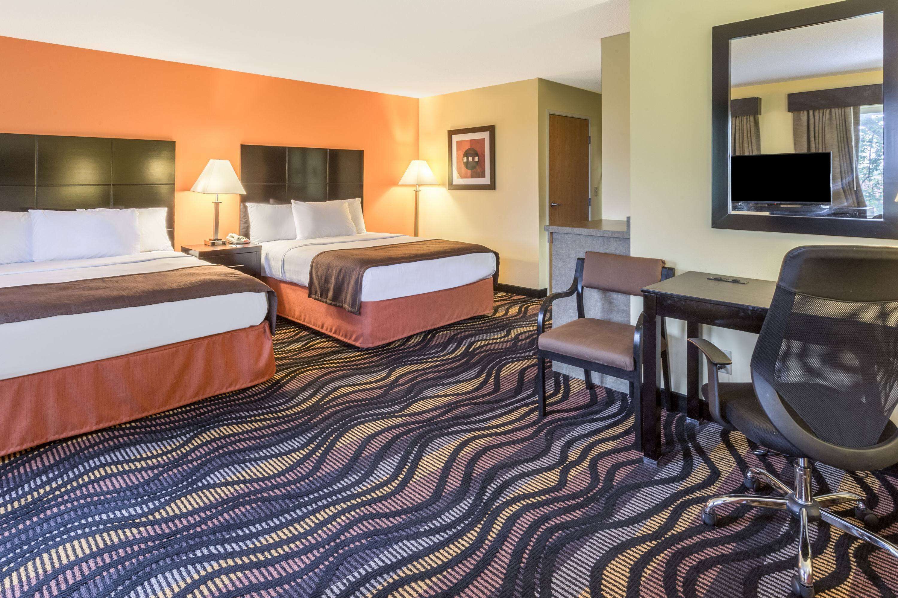 A hotel room with two beds, a desk, a chair, and a television.