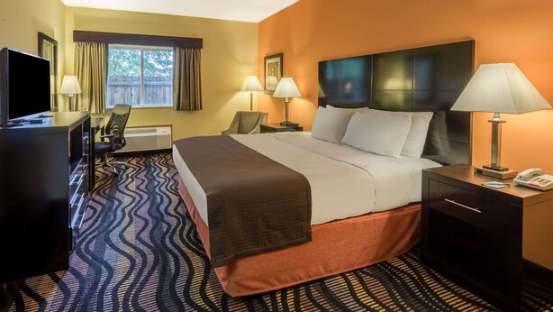 A hotel room with a bed, bedside tables, a desk with a television, and a window with curtains. - AmericInn by Wyndham Streator (Streator)