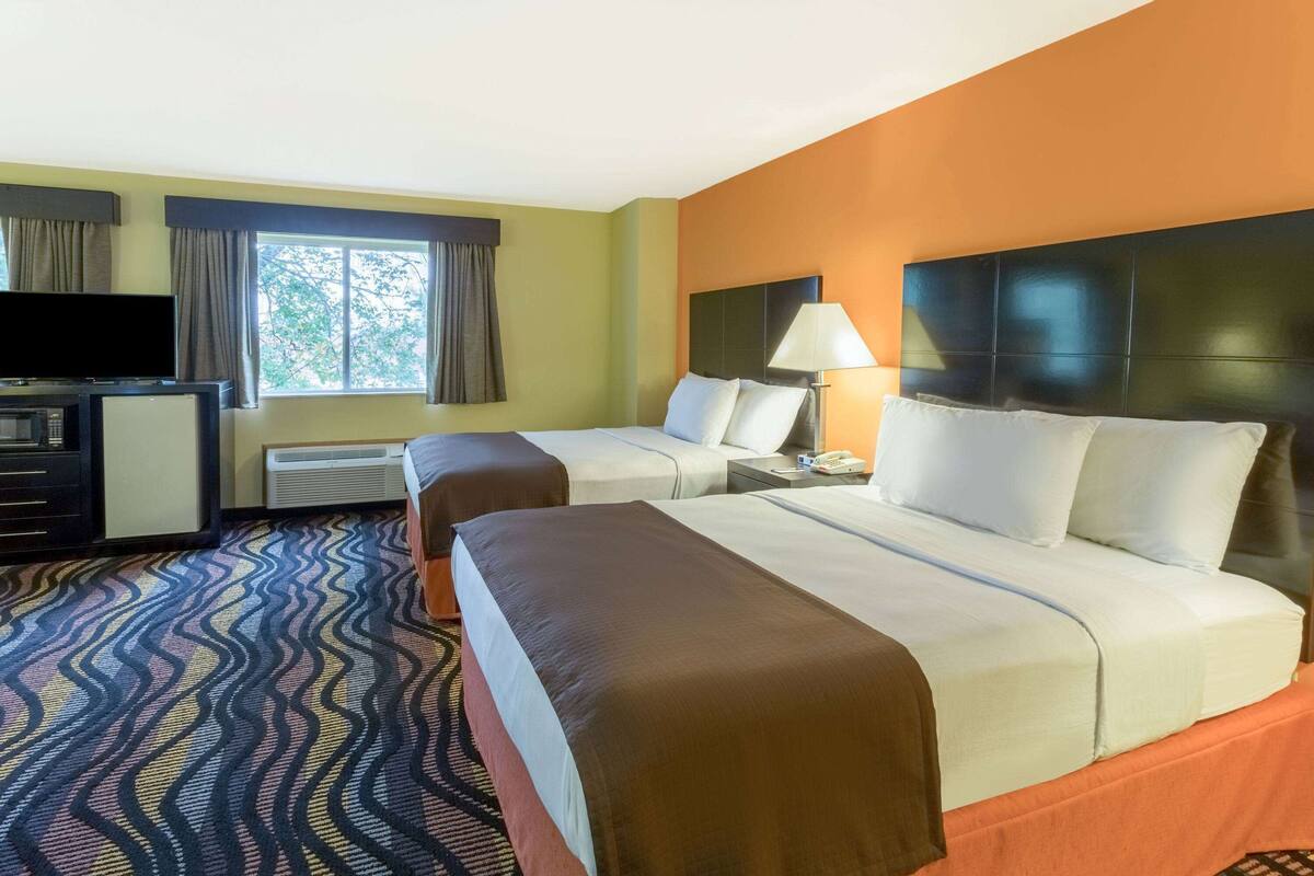 Une chambre d’hôtel avec deux lits, une télévision, un bureau et une fenêtre avec des rideaux.