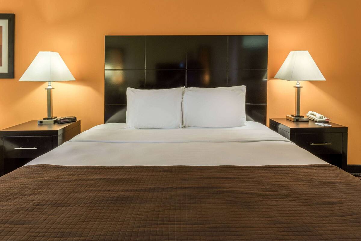 Une chambre d’hôtel avec un grand lit, deux tables de chevet, une petite table et un téléphone fixé au mur.