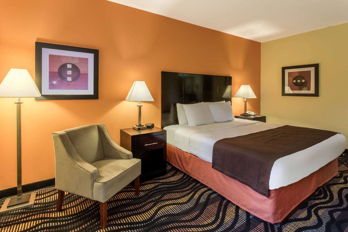 Une chambre d’hôtel comprenant un lit, deux tables de chevet, une chaise et deux lampes.