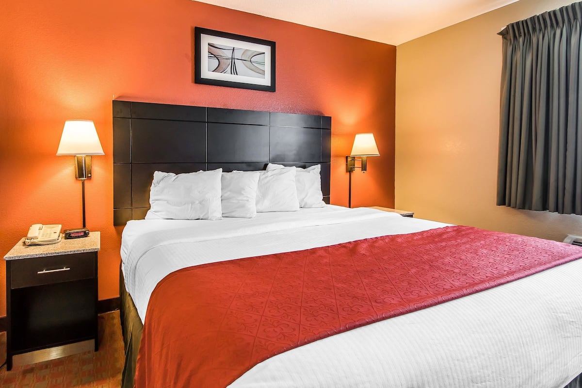 A hotel room with a large bed, two bedside lamps, a nightstand with a phone, and a framed picture on the wall.