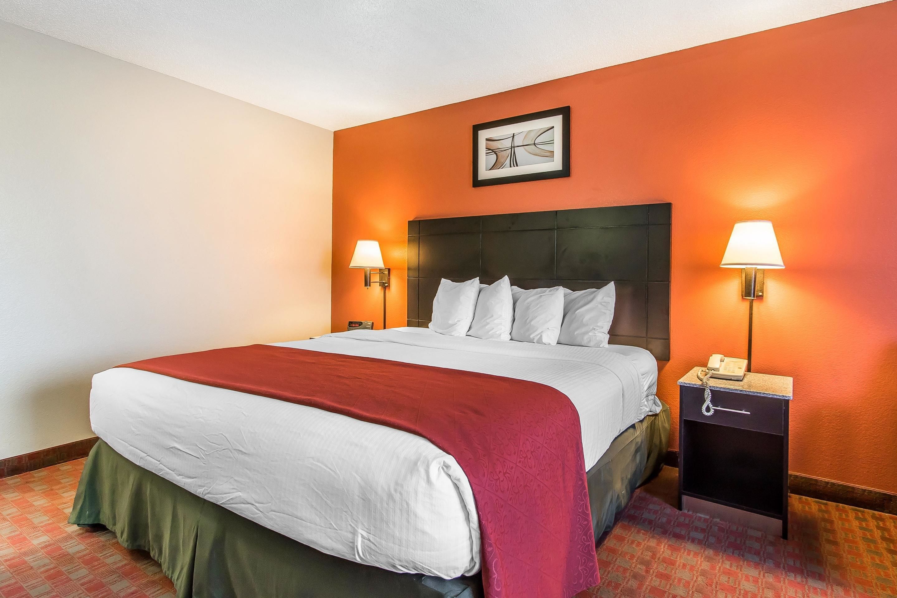 Una habitación de hotel con una cama grande, dos lámparas de noche, una mesita de noche con un teléfono y un cuadro en la pared.