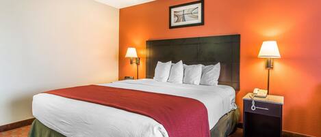 Una habitación de hotel con una cama grande, dos lámparas de noche, una mesita de noche con un teléfono y un cuadro en la pared.
