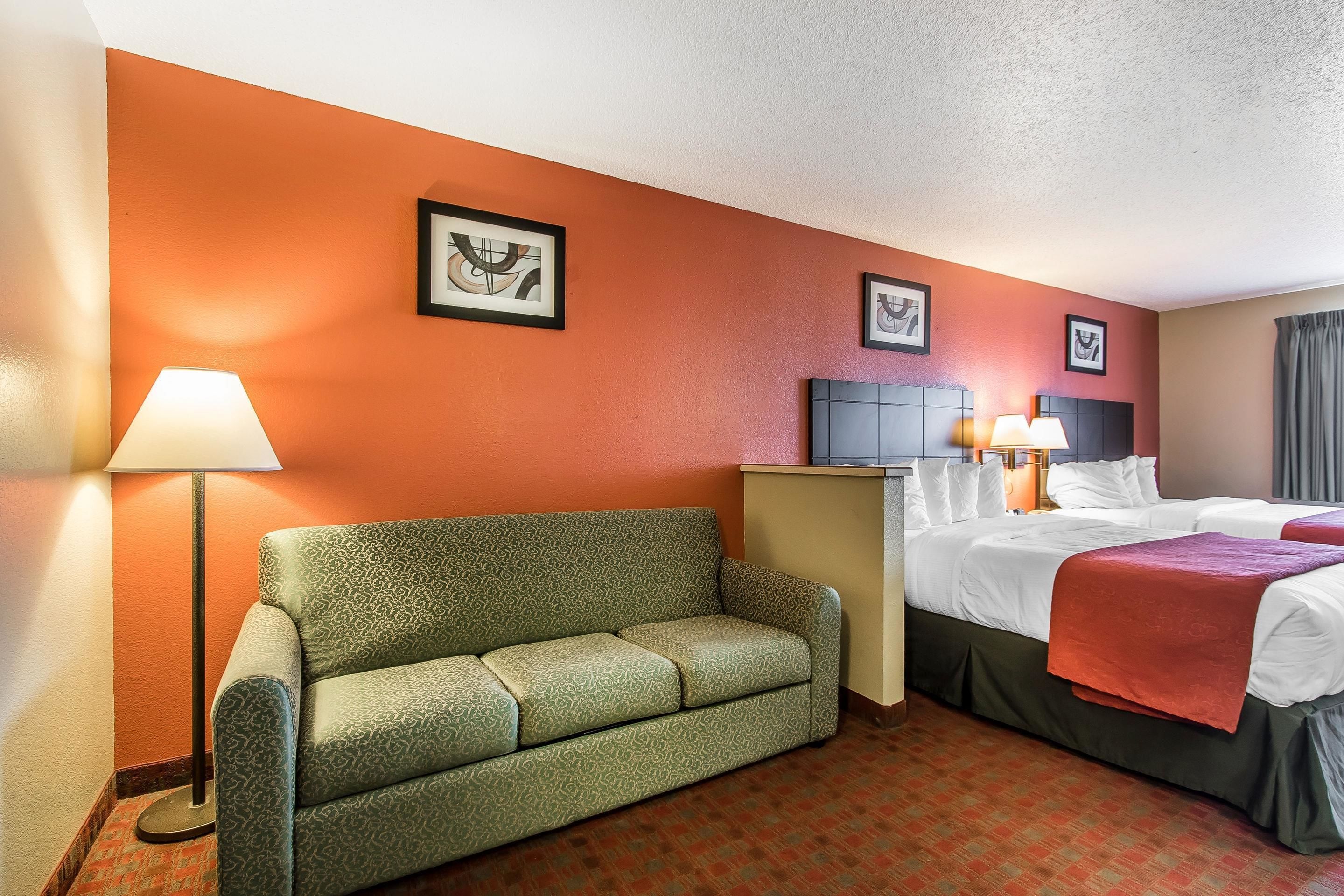 A hotel room with a green sofa, two beds with white linens, a desk, and a lamp.