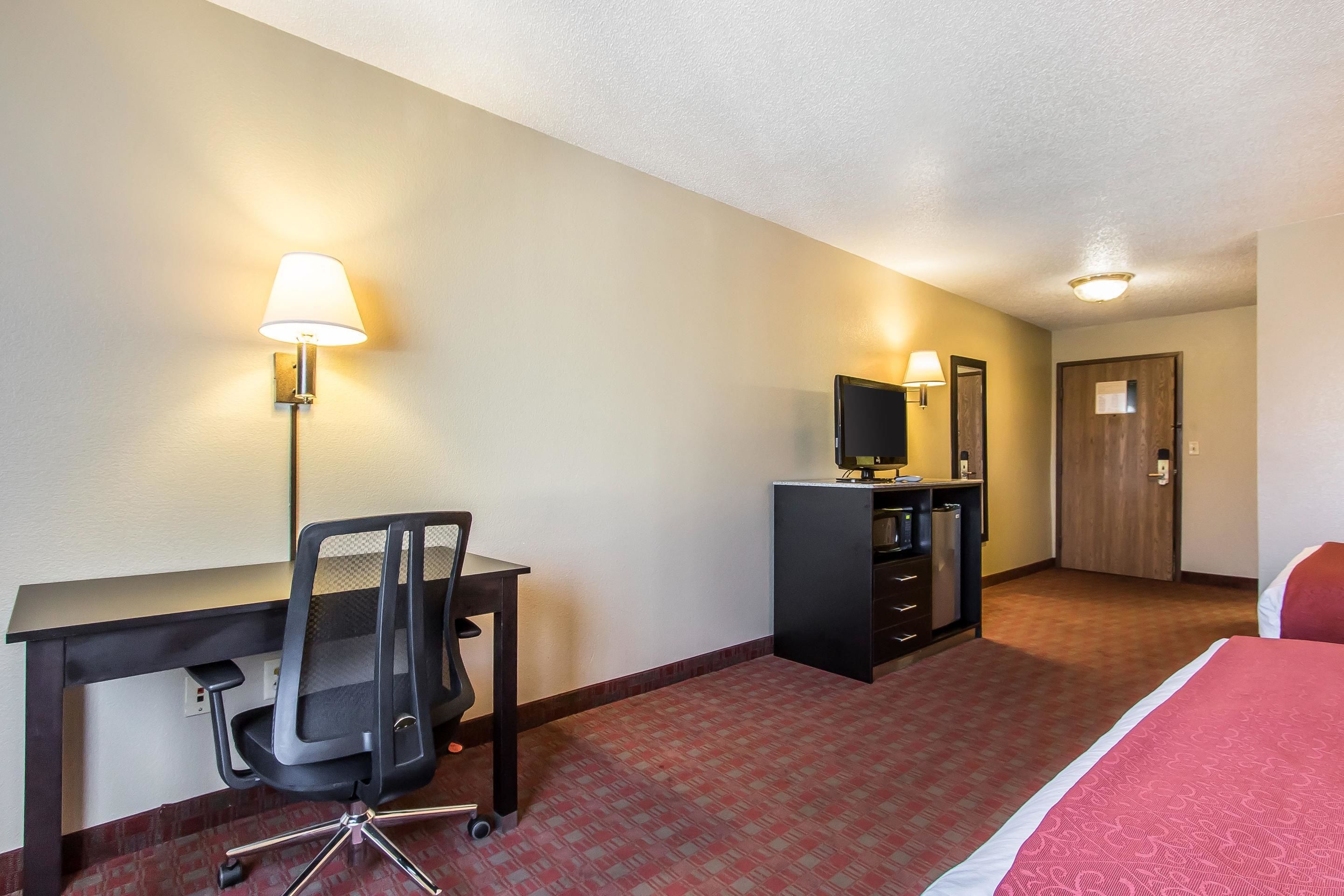 A hotel room with a desk, chair, television, wardrobe, and a bed.