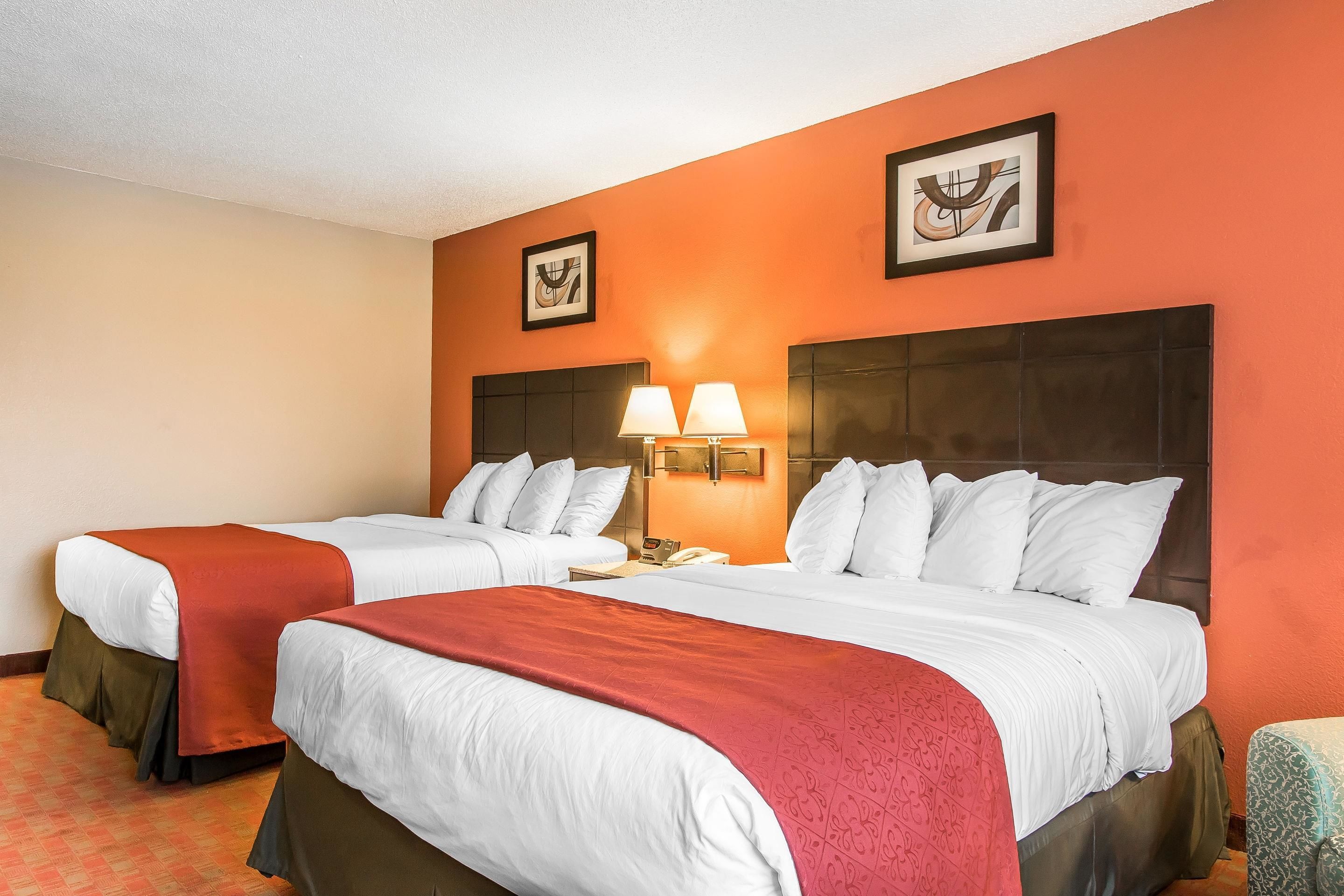 A hotel room with two beds, a red carpet, and a wall with framed artwork.