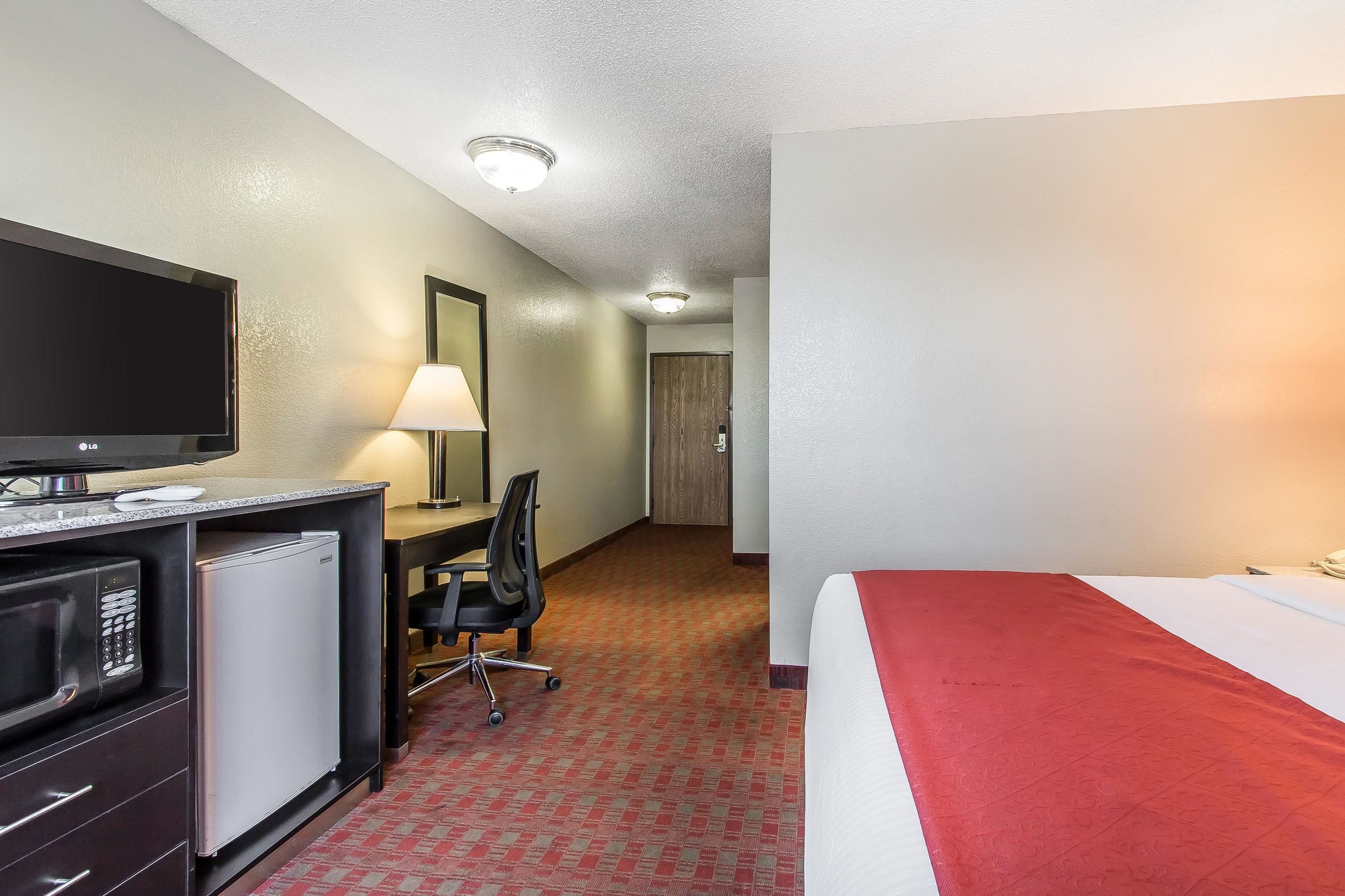 A hotel room with a bed, a desk with a computer, a microwave, and a TV.