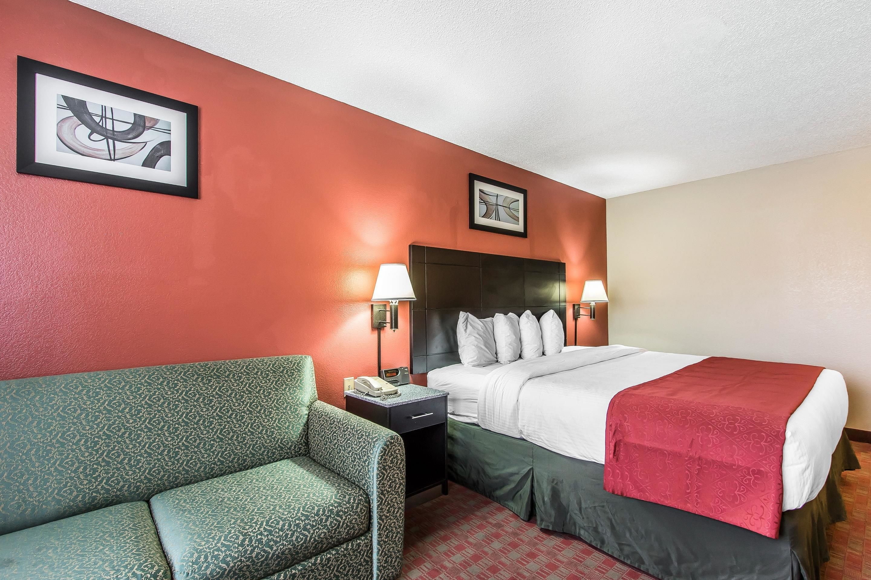 A hotel room with a bed, two bedside tables, a green sofa, and two wall-mounted lamps.