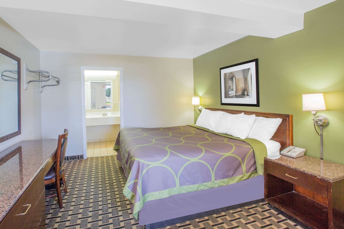 A hotel room with a bed, bedside table, lamp, and a mirror.