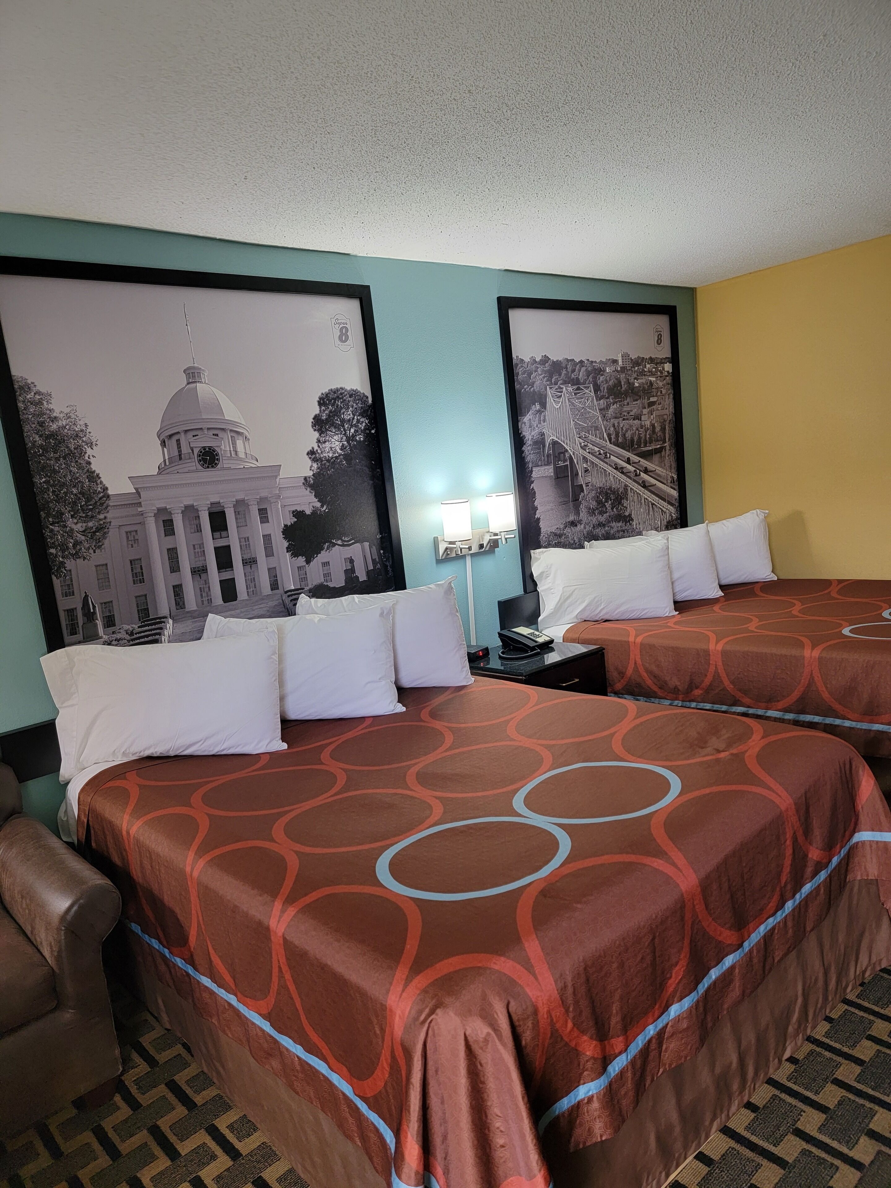 A hotel room with two beds, a nightstand, and a lamp.