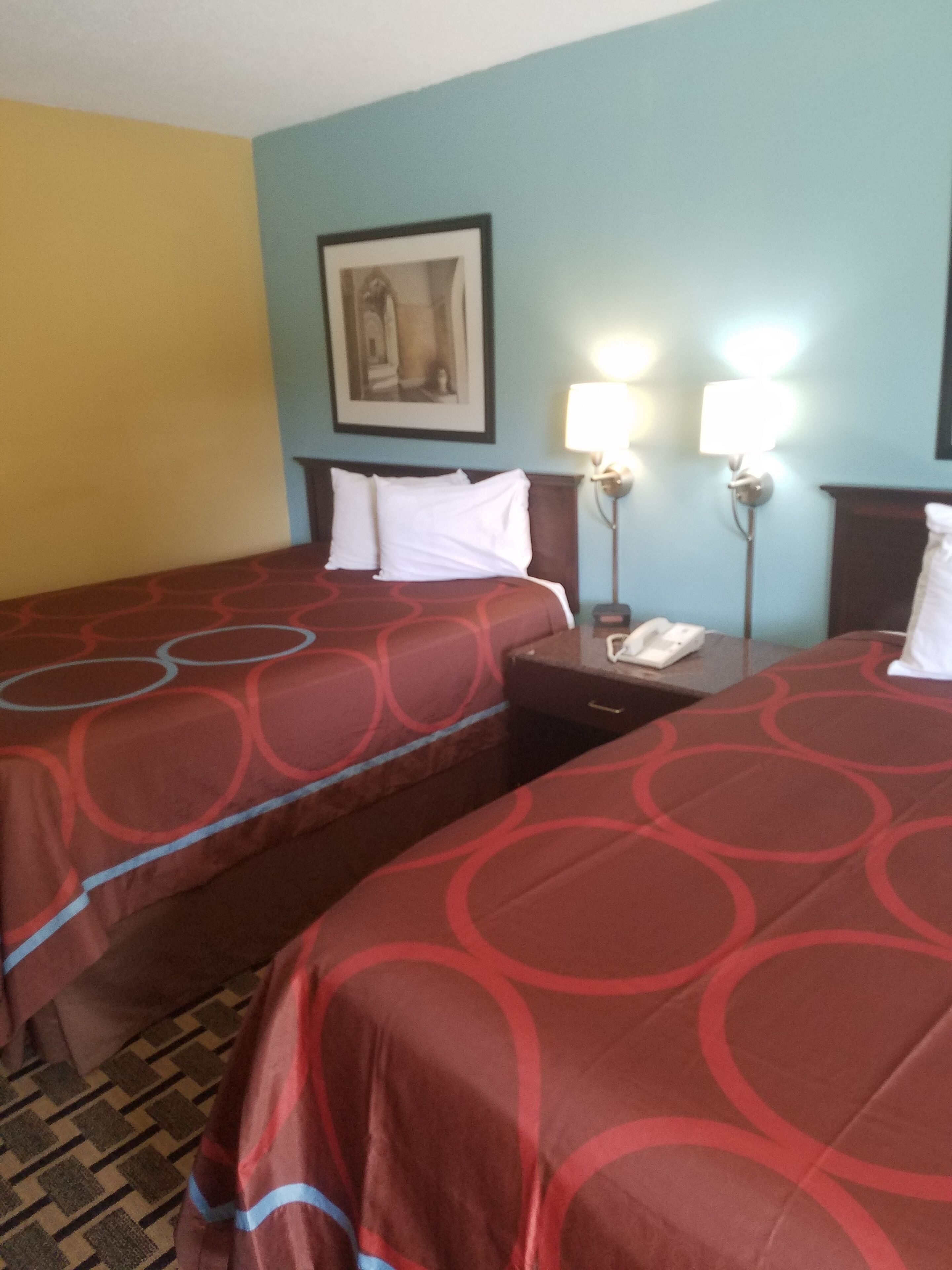 Una camera d'albergo con due letti, un comodino con il telefono e due lampade a parete.